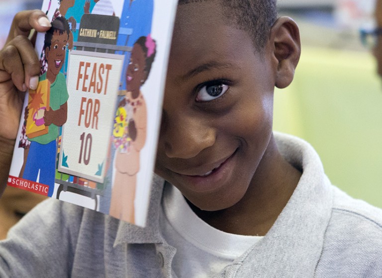 Little boy smiling holding up a book.
