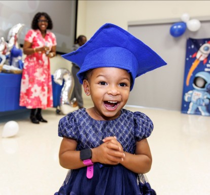 A little girl with a blue graduation cap smiles at the Nurse-Family Partnership graduation event in 2025.