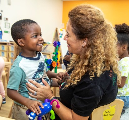 LIttle boy smiles while looking at a child care teacher.