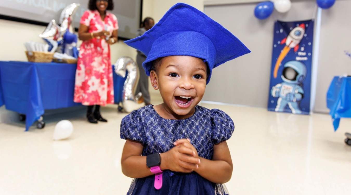 A little girl with a blue graduation cap smiles at the Nurse-Family Partnership graduation event in 2025.