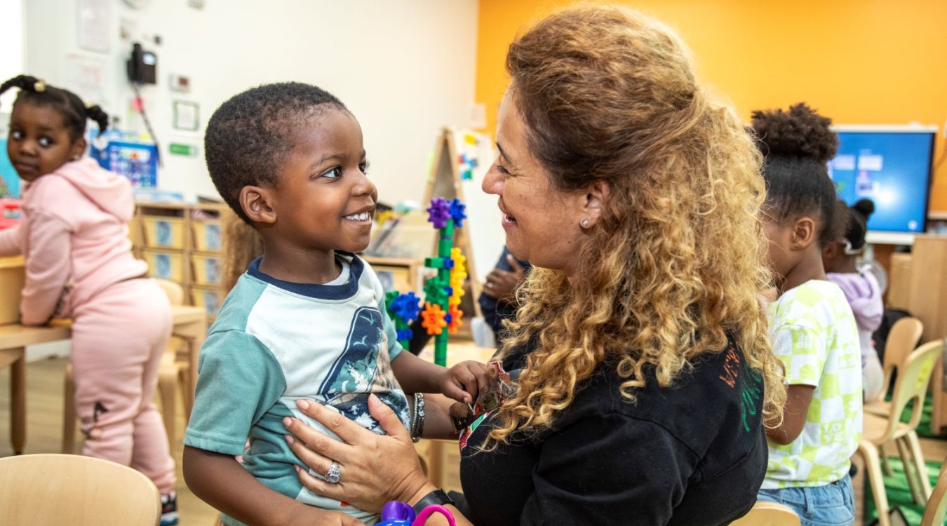 LIttle boy smiles while looking at a child care teacher.