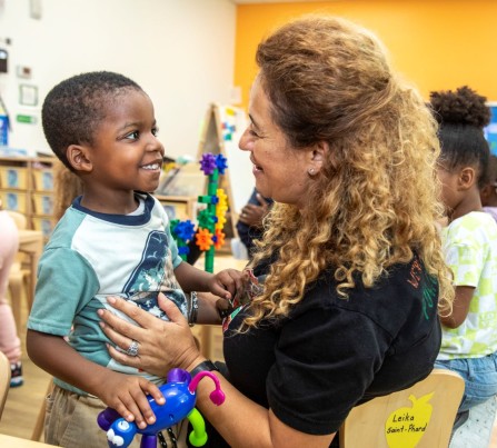 LIttle boy smiles while looking at a child care teacher.