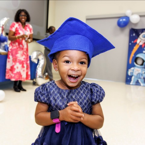 A little girl with a blue graduation cap smiles at the Nurse-Family Partnership graduation event in 2025.