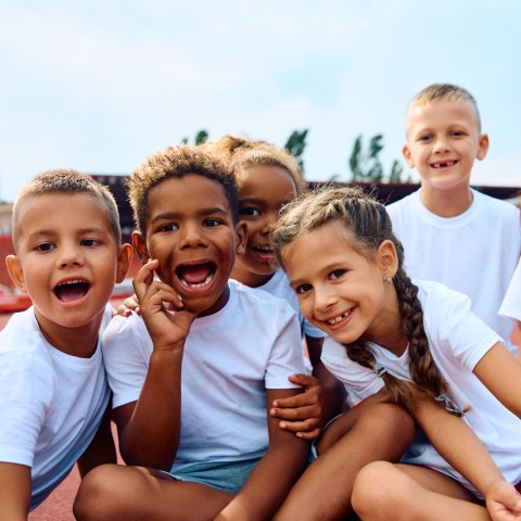 a diverse group of smiling children in white t-shirts.
