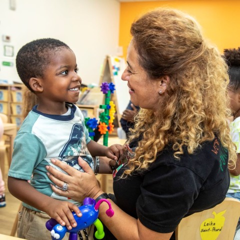 LIttle boy smiles while looking at a child care teacher.