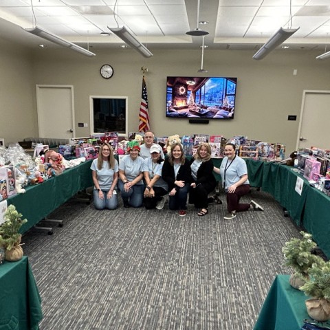 Members of the CSC Volunteering Committee kneel in front of tables full of toys for the first-ever Holiday Pop-Up Event in 2025.