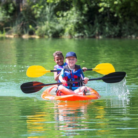 Two boys wearing life jackets in a kayak smiling while rowing through a river.